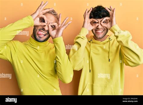 Homosexual Gay Couple Standing Together Wearing Yellow Clothes Doing Ok Gesture Like Binoculars