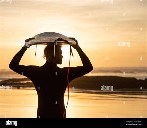 Silhouette Surfer Carrying Surfboard Over Head At Beach During Sunset