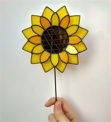 A Hand Holding A Stained Glass Sunflower On Top Of A White Wall With A