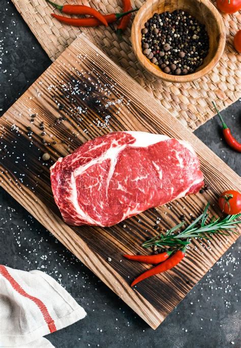 Raw Rib Eye Beef Steak On Wooden Board With Chili Pepper Salt And