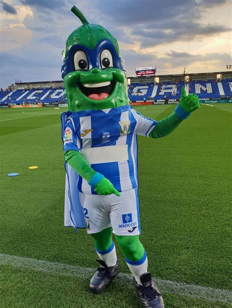 A Mascot Dressed In Blue And White Stands On A Soccer Field With His