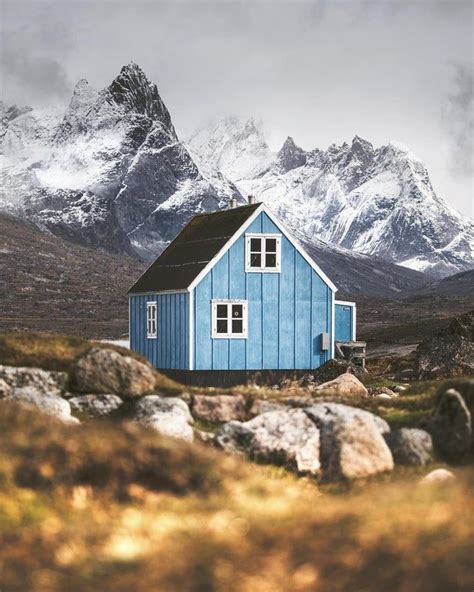 a small blue house sitting on top of a rocky hillside next to snow ...