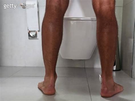 Rear View Leg Of Man Standing Peeing To Toilet Bowl In Restroom At Home