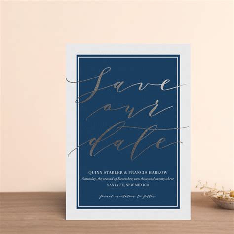 A Blue And Gold Foil Save The Date Card On A Wooden Table Next To A Potted Plant