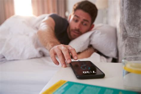 Homem Acordando Em Alcance Da Cama Para Desligar O Alarme No Telefone