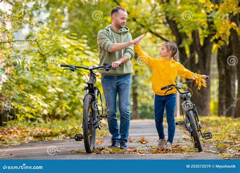 Happy Father And Daughter Walk With Bicycles In The Autumn Park On A