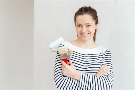 Premium Photo Young Woman Painting The Wall With Paint Roller And Brush