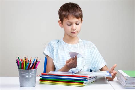 Garçon S asseyant Au Bureau Avec La Pile Des Livres Et Des Carnets D