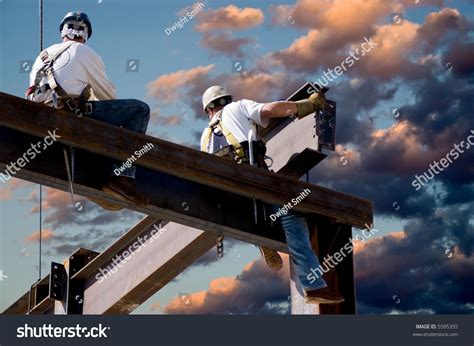 Two Ironworkers Atop The Skeleton Of A Modern Building One Man Is