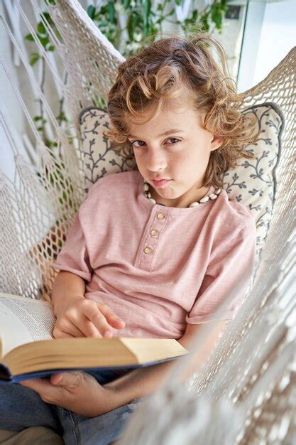 Niño con libro acostado en hamaca y puchero labios Foto Premium