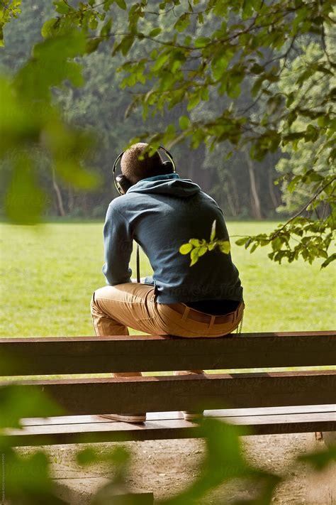 Young Man Sitting On A Bench In A Park Listening To Music By Stocksy