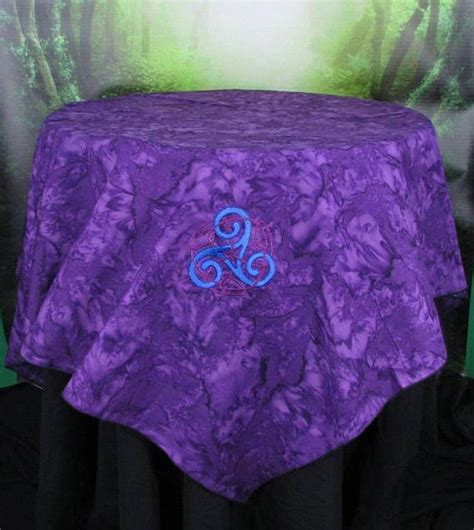 a purple table cloth with a blue monogram on the front and bottom, sitting in front of a green ...