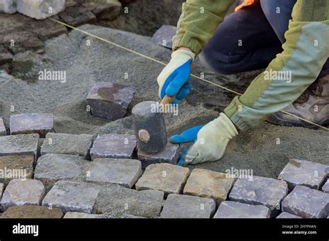 Worker Using Rubber Hammer To Laying Pavement Stones On Sidewalk Near