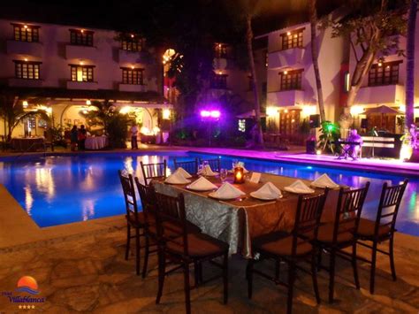 An Outdoor Dining Area Next To A Swimming Pool At Night With Lit