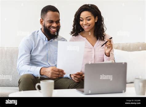 Cheerful Black Couple Reading Documents At Home Checking Agreement