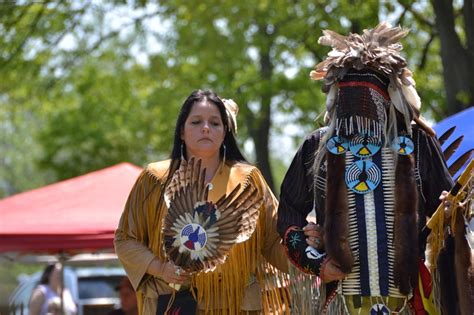 Two People Dressed In Native American Clothing Standing Next To Each Other