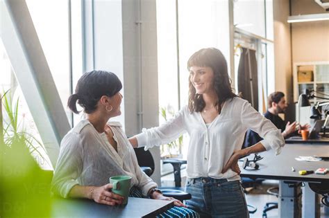 Female Coworkers Smiling While Talking At Counter In Office Stock Photo