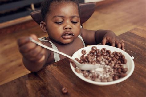 Cereal para niños negros y comer bebé en una cocina casera con comida y