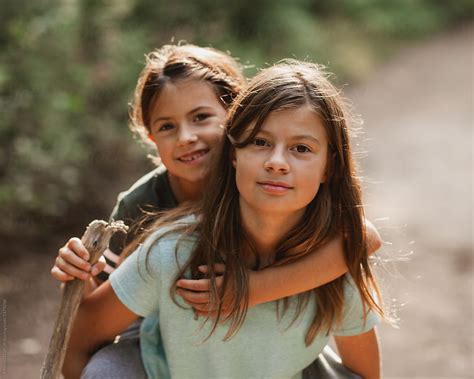 «Big Sister Giving Piggy Back Ride To Little Sister While On Hike» de