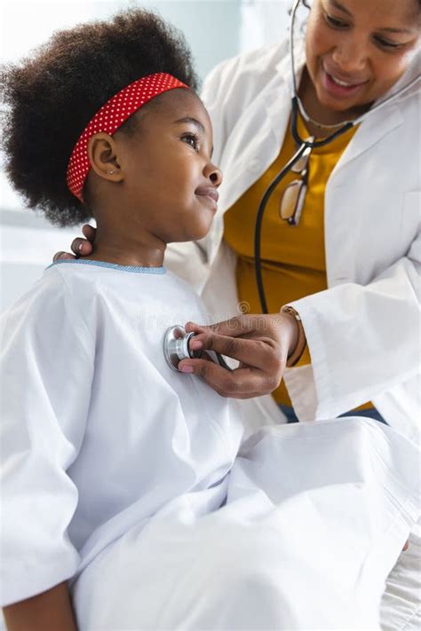 African American Female Doctor Examining Girl Patient Using Otoscopy At