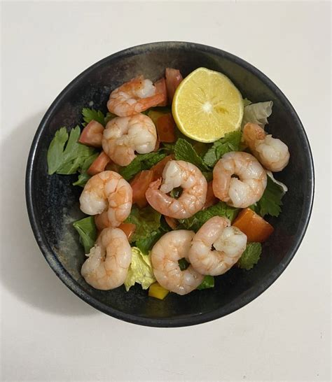 A Black Bowl Filled With Shrimp And Lettuce