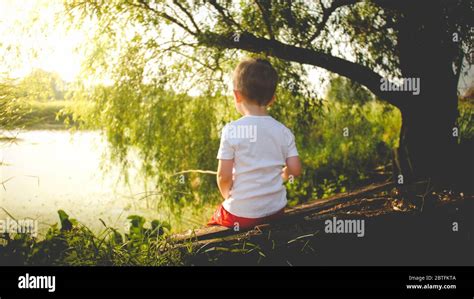 Toned Rear View Photo Of Little Boy Fishing On The River At Sunset