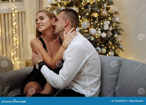 Couple In Love Kisses And Hugs On The Sofa Near The Christmas Tree