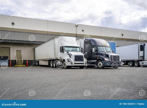 Black And White Big Rigs Semi Trucks With Semi Trailers Loading Cargo