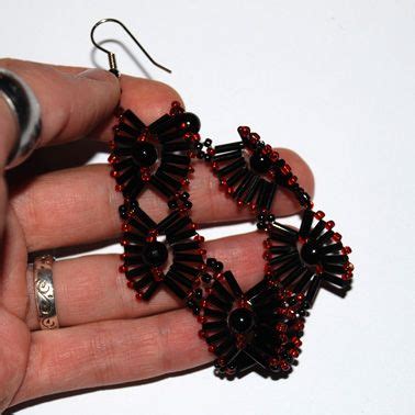 a pair of red and black beaded earrings being held by someone's hand