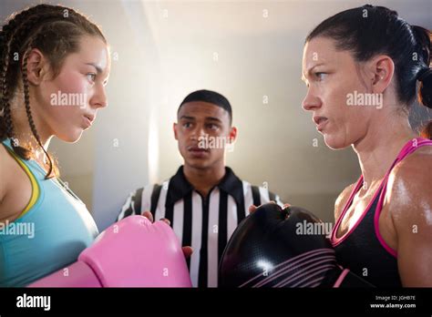 Young Female Boxers Looking At Each Other Against Referee At Fitness