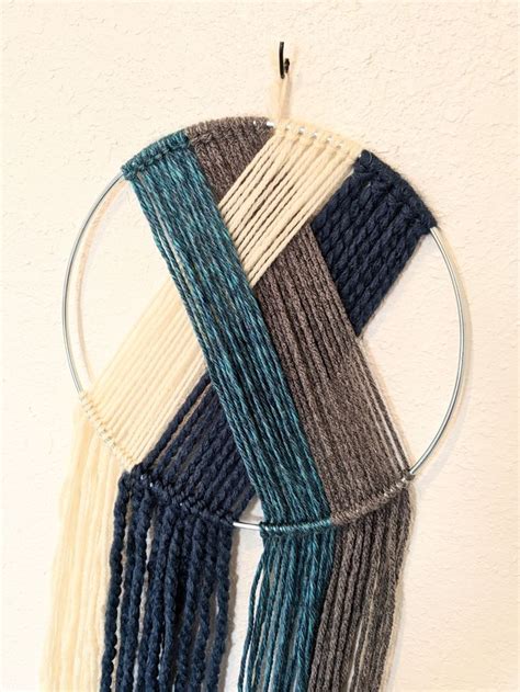 A Wall Hanging Made Out Of Yarn On A White Wall With A Circular Metal Frame