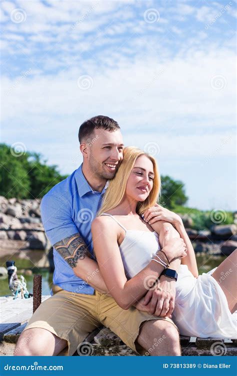 Happy Romantic Young Couple Sitting On The Pier And Enjoying Sea Stock