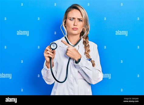 Beautiful Young Blonde Doctor Woman Holding Stethoscope Pointing With