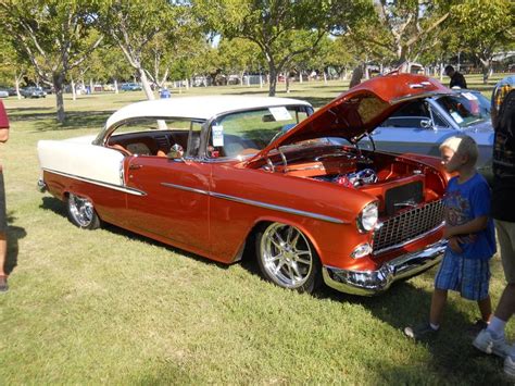 An Old Red Car Parked In The Grass With People Looking At It And Two