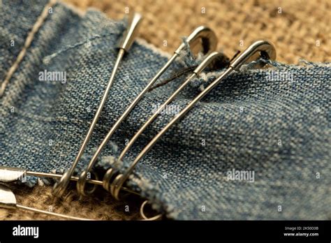 Safety Pins On A Strip Of Denim Against A Homespun Fabric With A Rough