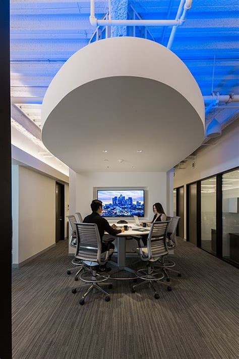 Two People Are Sitting At A Table In An Office Setting With A Large Screen On The Wall