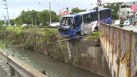 Micro ônibus bate e fica pendurado à beira de córrego na Grande SP