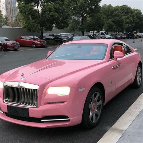 a pink rolls royce parked in a parking lot next to a sidewalk with cars ...