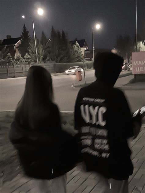 Two People Are Walking Down The Street At Night With Their Backs To