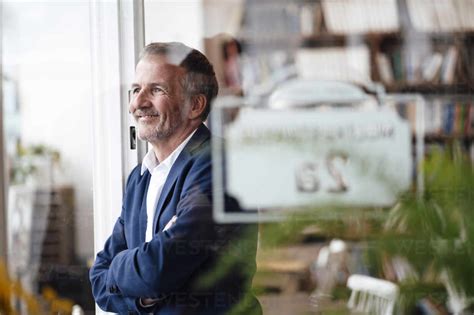 Lächelnder Geschäftsmann mit verschränkten Armen der durch ein Fenster