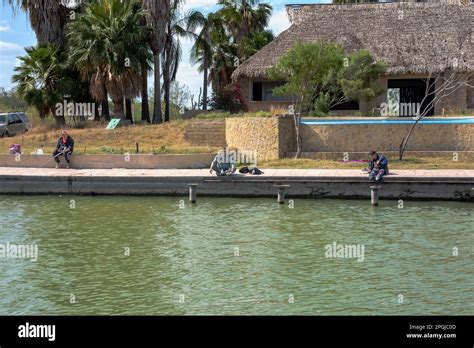 Three people sit along the Rio Grande River on the Mexican side of the river, US/Mexico border ...