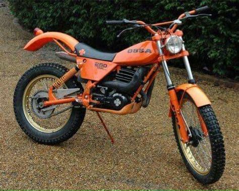 An Orange Dirt Bike Parked On Top Of A Gravel Road Next To A Green Bush