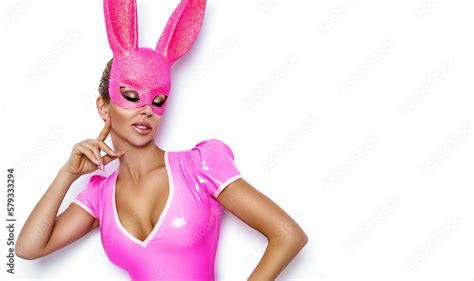 Sexy Blonde Woman Is Posing In Latex Easter Bunny Costume And Pink Bunny Mask On White