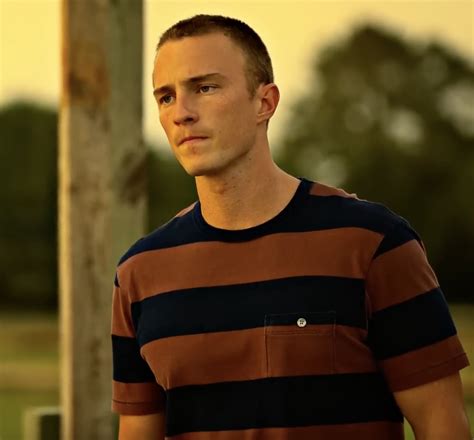 A Man Standing Next To A Pole In A Field With Trees And Grass Behind Him