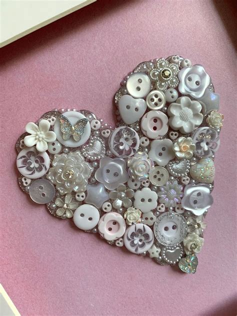 A Heart Made Out Of Buttons Sitting In A Box On Top Of A Pink Surface