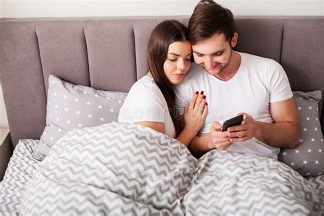 Smiling Young Couple Taking Selfie Together In Bedroom Stock Image