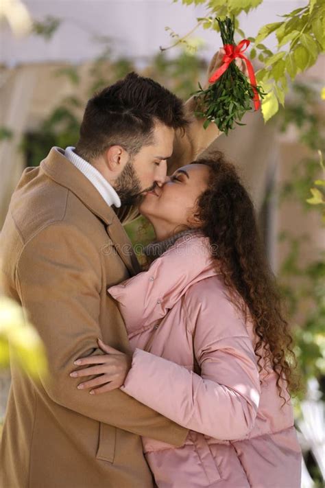 Happy Man Kissing His Girlfriend Under Mistletoe Bunch In Room