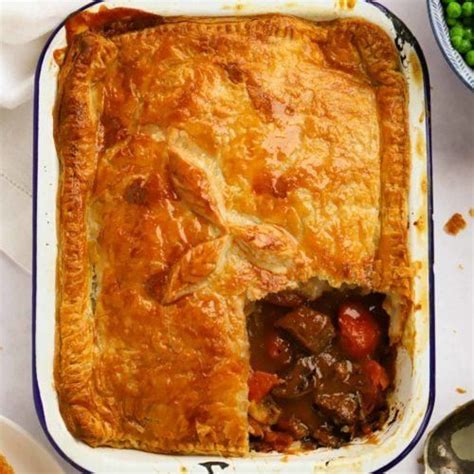 A Pie With Meat And Vegetables In It On A Table Next To Bowls Of Peas