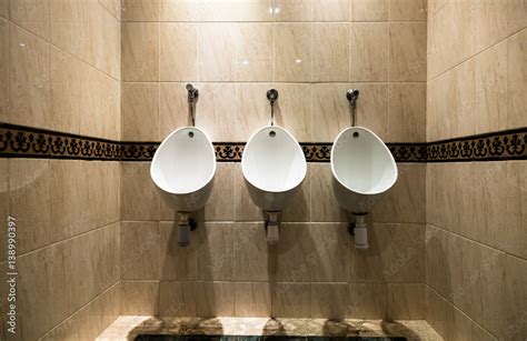 Three Bright White Urinals Fitted To Wall Covered With Light Brown