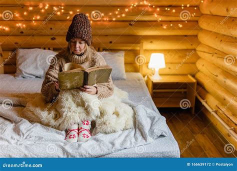 Adult Woman Relaxing On Cozy Bed In Log Cabin In Cold Winter Stock